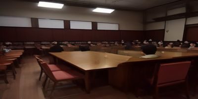 日本商务会议场景，穿着正装的职场人士在玻璃幕墙会议室内用日语进行商务汇报，投影屏幕展示数据图表